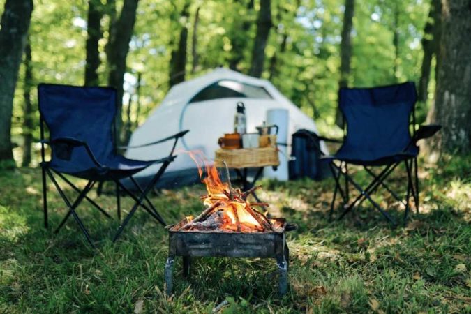 Epic camping setup with glowing campfire, tent and chairs in peaceful forest setting