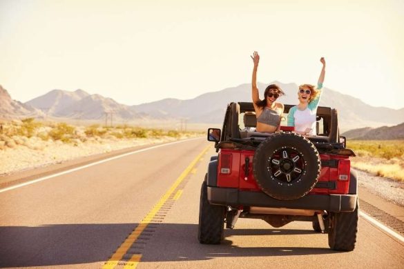 Two friends celebrating in red jeep on desert highway with mountains in background