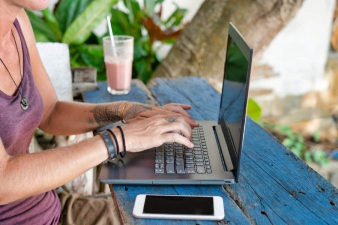 Digital nomad working on laptop at outdoor cafe with tropical plants and smoothie