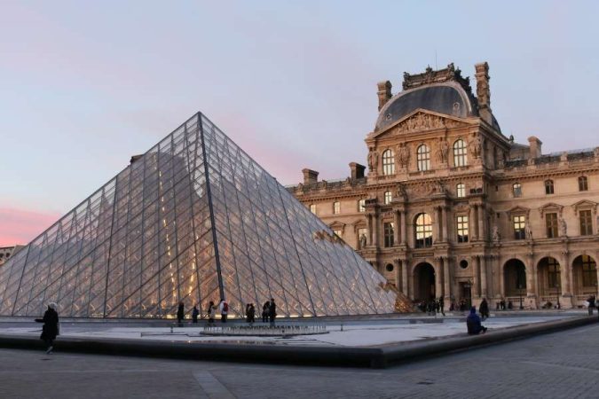 Glass pyramid entrance of famous Parisian museum at twilight with classical architecture backdrop