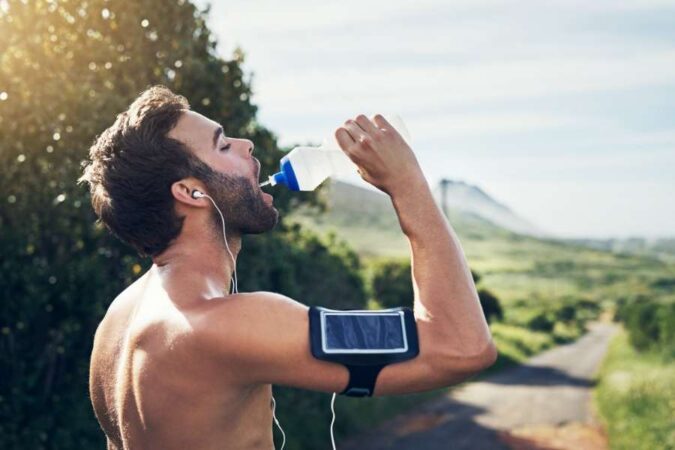 A fitness runner drinking water to stay hydrated during extreme heat outdoors.